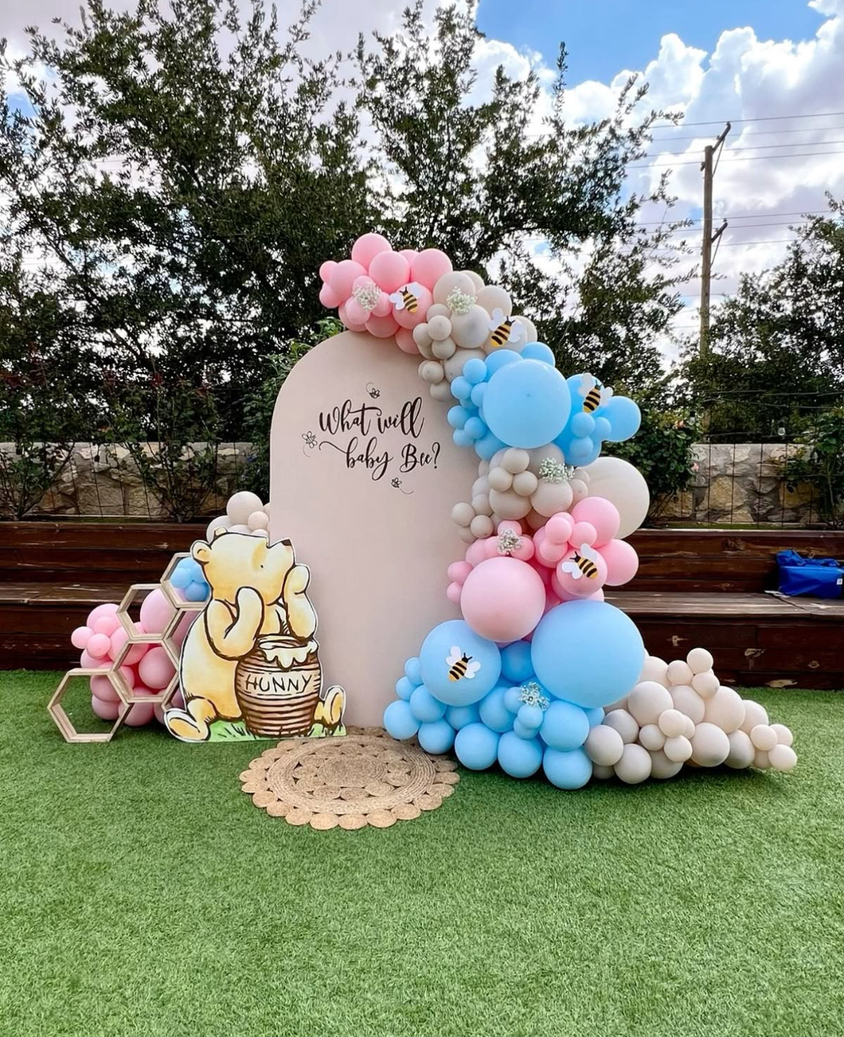 What Will Baby Bee gender reveal backdrop with Winnie the Pooh cutout and pink, blue and cream balloon garland